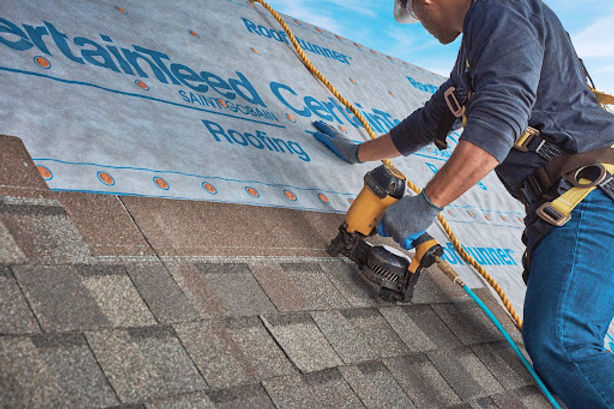 Roofer installing shingles with a CertainTeed banner